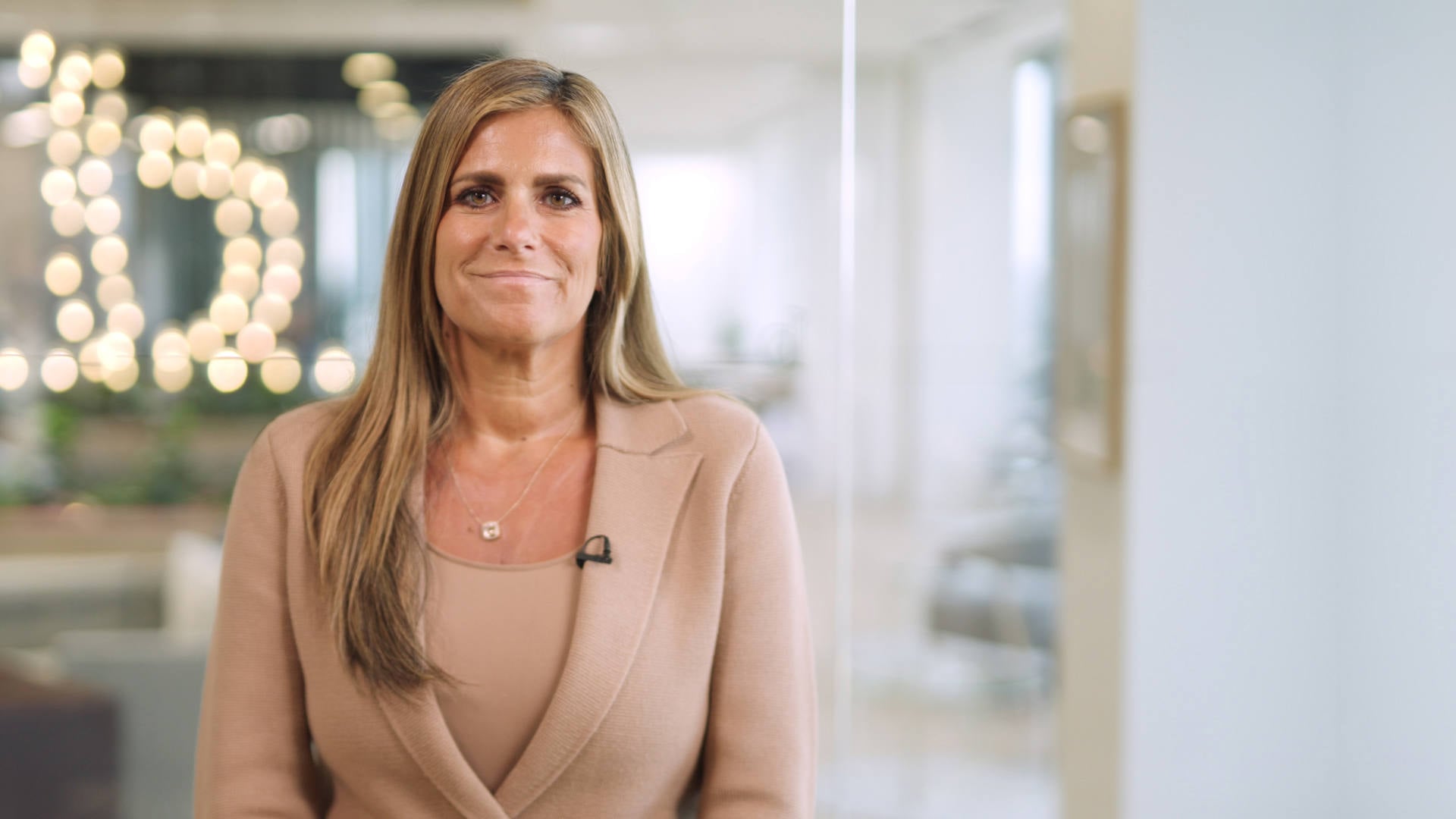 A woman dressed in a business suit stands by a window, exuding professionalism and determination in a corporate setting.